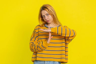 Bluzlu, beyaz bir kadının mola verme hareketi yapması, sınır veya dur işareti göstermesi, baskı yok, daha fazla zamana ihtiyacım var, dinlenmeye ihtiyacım var, yardım. Sarı arka planda izole edilmiş genç bir kız.