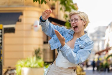 Neşeli, zengin, mutlu bir kadın el hareketi yaparak para harcıyor, daha fazla bahşiş kazanıyor, büyük kar ediyor, piyango kazanıyor, paylaşıyor, dışarıda kutluyor. Genç sarışın bayan gezgin şehir caddesinde duruyor..