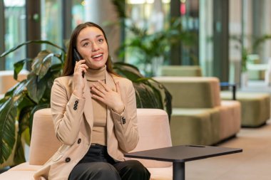 Telefon, iyi haber, dedikodu. Kafkasyalı genç iş kadını mutlu bir sürpriz. Akıllı telefondan hoş sohbetler ediyor. Modern ofis lobisinde arkadaşıyla eğleniyor. Otel odasında oturan bayan.
