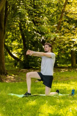 Sportif formda bir adam parkta yoga yaparken spor minderinde nefes egzersizi yapıyor. Ellerinizi kaldırın. Koşucu dışarıda egzersiz yapmaktan hoşlanıyor. Aktif sporcu motivasyonu. Aktif sporcu sağlıklı yaşam tarzı.
