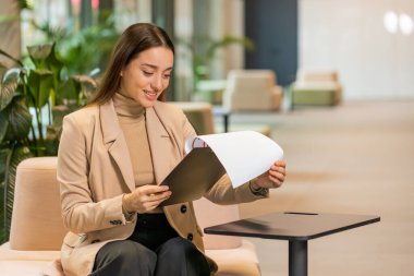 Beyaz tenli genç iş kadını belgelerle çalışıyor, bilgileri analiz ediyor, gazete okuyor mali raporları hazırlıyor. Genç bayan girişimci ofis lobisindeki grafik belgelerini analiz ediyor..