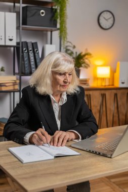 Üst düzey iş kadını, internet video dersine ya da ofis masasındaki bilgisayar toplantısına katılırken not alıyor ya da not alıyor. Kız bağımsız büyükanne destek hizmetleri webcam 'e bakıyor.