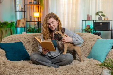 Genç, rahat, Kafkasyalı, kızıl saçlı kadın evde koltukta köpeğe kitap okuyor. Yumuşak bir sesi ve sıcak bir gülümsemesi var. Evcil hayvan sessizce onun yanında uzanıyor, sakince dinliyor ve günün sonunda nazik bağlantılarını paylaşıyor..