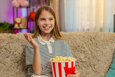 Genç kız patlamış mısır yer ve kanepede oturup eğlenirken televizyonda komik çizgi filmler izler. Okullu çocuk evde rahat bir film izlerken keyifli ve rahat görünüyor.