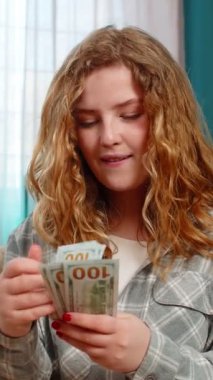 Genç bir kadın heyecanla elinde nakit dolarları sayıyor gülümsüyor ve beklenmedik mali kazancı kutluyor. Kanepedeki beyaz saçlı kız piyango kazanmasından, maaşından ya da sürpriz parasından memnun.