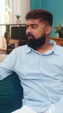 Evde oturan Hintli adam, akıllı telefon hatasından sonra alnına tokat atıyor. Pişman olmuş görünüyor. Kanepedeki Arap adam başını eğiyor. Yüzü ekşiyor. Hata reaksiyonu..