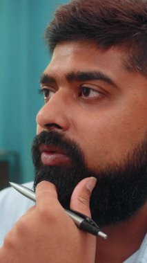 Evindeki Hintli adam kalemini elinde tutuyor. Dikkatlice ileriye bakıyor ve odaklanmış bir zihinle görevler planlıyor. Yakın plan Arap adam bir sonraki hamle ve stratejik fikirler üzerinden kalem çevirme hedefleri düşünüyor