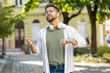 Ciddi derecede tatminsiz, gözlüklü, dışarıda duran, sinirli bakışları olan, geç kaldığı için üzülen, kol saatine dokunan, sinirli birini arayan, beyaz bir turist.