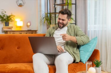 Tartışma. Öfkeli, sinirli, serbest çalışan genç adam koltukta oturmuş hararetli sohbetlere dalıyor. Kafkasyalı erkek, apartman odasındaki kanepede dizüstü bilgisayar kullanarak hayal kırıklığı yaşıyor..