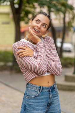 Düşünceli gülümseyen, düşünceli, mutlu, genç, yetişkin bir kadın. Çözüm üzerinde kafa yoran, soru soran, ilham veren açık havada rüya gören. Şehir sokağındaki güzel kız. Kasaba yaşam tarzları.