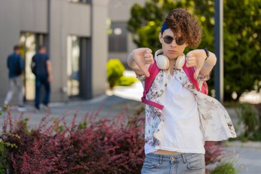 Hoşlanmamak. Güneş gözlüklü üzgün genç adam işaret dilini gösteriyor hoşnutsuzluğunu, hoşnutsuzluğunu, tatminsizliğini, kötü işini, hatasını gösteriyor. Şehir Güneşi Sokağı 'nda hoşnutsuz bir adam..