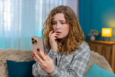 Evde endişeli bir şekilde önemli bir mesaj bekliyor. Akıllı telefonu kaydırırken tırnağını yiyor. Kanepede oturan beyaz saçlı kız gergin, stresli, duygusal beklenti, gerilim anı