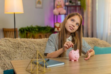 Küçük bir kız çocuğu, evdeki kanepede oturmuş gülümserken kumbaraya bozuk para koyuyor ve gururlanıyor. Okul çocuğu yeni bir oyuncak almak için para biriktiriyor, erken sorumluluk ve neşe alışkanlıkları gösteriyor.