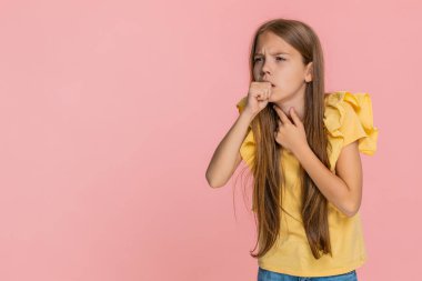 Genç kız boğaza dokunuyor ve üzgün bir suratla kaşlarını çatarken nazikçe öksürüyor. Boğaz ağrısı ve hastalıkla ilgili rahatsızlık belirtileri gösteriyor. Pembe arka planda izole edilmiş okul çocuğu.