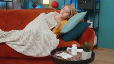 Kafkasyalı ergen çocuk evde hasta. Kanepede termometreyle yatmak, yüksek ısıyı kontrol etmek, üzgün ve yorgun, yakınlarda ilaç paketleri, bir oturma odasında hastalık ve yorgunluk duyguları sergilemek.