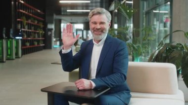 Hoş geldiniz. Kafkas 'lı mutlu iş adamı el sallayarak selam veriyor. Birine hoş geldin diyor. İnternetteki Webinar, uzaktan konuşma. Takım elbiseli girişimci adam modern ofis lobisinde oturuyor..
