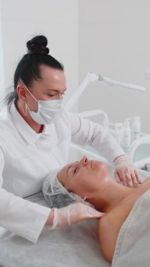 Kozmetik uzmanı özel nemlendirici krem uyguluyor, güzel beyaz bir kadının yüzünü ovuyor, soyuyordu. Güzellik salonunda yüz bakımı yaşlanmayı önleyen kozmetik masaj prosedürü. Güzellik tedavisi