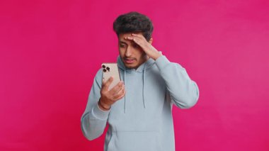 Üzgün Hintli adam akıllı telefon daktilo kullanıyor, oyun oynuyor, kaybediyor, piyango aniden şaşırıyor kötü şans kaybı şanssız haber. Arap Hindu sakallı adam pembe arka planda izole edilmiş.