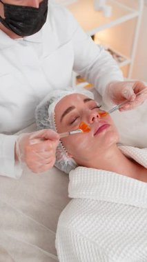 Enzim terapisi. Güzellik uzmanı, genç yetişkin bir kadının yüzüne nemlendirici kimyasal krem maske takıyor. Kaplıcadaki kız cilt bakımı. Yüz kozmetolojisi tedavisi. Dikey