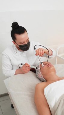 Kozmetik doktoru kadınları mikro akıntıya maruz bırakıyor. Spa kliniğinde anti-yaş kız cilt bakımı. Güzellik uzmanı, yüz kozmetik güzellik tedavisi için elektriksel impulslar kullanıyor. Dikey