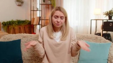 Genç yetişkin bir kadın evdeki kanepede otururken elini sallayarak internetten gelen olumsuz mesaja tepki veriyor. Sarışın kız hayal kırıklığı, anlaşmazlık, duygusal protesto ve hoşnutsuzluk gösteriyor.