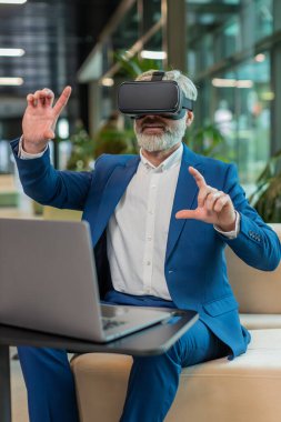 Olgun bir iş adamı yazılım geliştiricisi kulaklık uygulaması kullanarak sunum yapıyor. Sanal gerçeklik 3D 360 videosu izliyoruz. Ofis lobisinde çalışan, VR gözlüklü, beyaz saçlı, takım elbiseli adam..