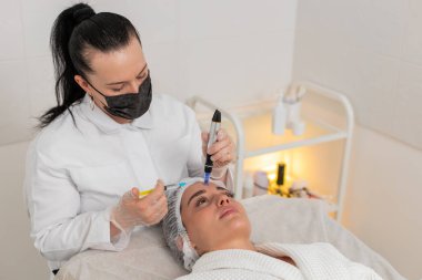 Kafkas kadın, kısmi mezoterapi seansı sırasında göz altında mikro tedavi görüyor. Kozmetik uzmanı serumu dermapen ile uyguluyor ve güzellik kliniğine enjeksiyon hazırlıyor..