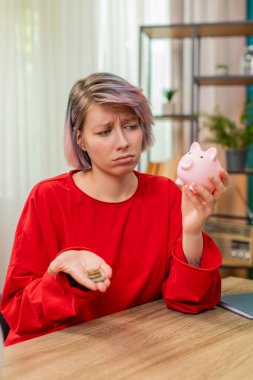 Mutsuz genç bir kadın, kumbaradaki bozuk paraları sayıyor evde oturmuş, hayal kırıklığına uğramış bir şekilde iç çekiyor. Finansal sıkıntı ve hayal kırıklığı gösteren beyaz bir kız yetersiz tasarruf konusunda endişeli..