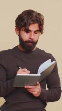 Düşünceli genç Hintli işadamı notlar alıyor, not defterine kalemle düşünceler yazıyor, liste yapmak için, iyi fikir. Latin kökenli yetişkin adam bej renkli stüdyo arka planında izole edilmiş.