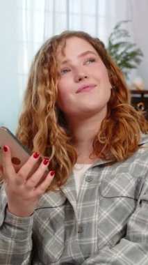 Genç bir kadın akıllı telefondan eski fotoğrafları çekerken mutlu geçmişi hatırlarken kendini nostaljik hissediyor. Kafkasyalı kızıl saçlı kız huzurlu duygusal yüzüyle kanepede oturuyor, sessiz bir anı anı yaşıyor, gülüyor.