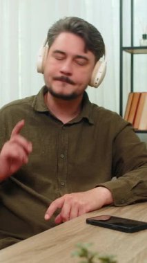 Evde orta yaşlı bir adam akıllı telefon kulaklıklarıyla müzik dinliyor. Kafasını sallıyor, içeriği gevşetiyor. Masadaki genç yetişkin adam ritmi sever. Gülümserken ses neşeli ve rahatlatıcı titreşimler getirirken.