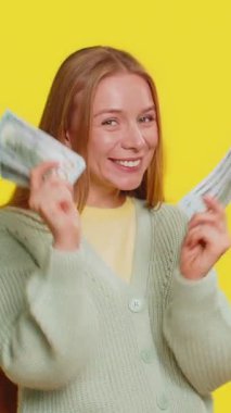 Zengin, mutlu, orta yaşlı, dans eden beyaz bir kadın elinde dolar banknotlarıyla hayranı, başarılı bir iş piyangosunun kazananı gibi para sallıyor. Sarı arkaplanda izole edilmiş kız