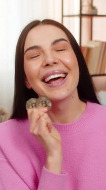 Evdeki genç kadın, yatırım yapmayı düşünen düşünceli bir şekilde altın BTC şifreli para çeviriyor. Kanepede oturan beyaz kız kripto piyasasını, kar fırsatlarını, finansal tercihleri analiz ediyor.