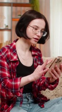 Genç kadın evdeki koltukta akıllı telefona bakıyor, iyi haberler aldıktan sonra sevinçle tepki veriyor ve piyango kazanıyor. Kız online piyangoyu zafer jesti, görünür mutluluk ve memnuniyet ile kutluyor.