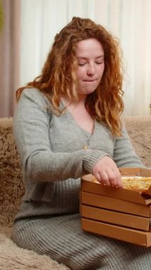 Hamile genç bir kadın evde pizza kutusunu açıyor, istekli bir ifadeyle bir dilim alıyor, lezzetli bir ısırık alıyor. Kız, küçük mutluluk ve memnuniyet anlarını kucaklayarak, konforlu yiyeceklerden hoşlanır..