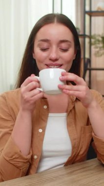 Genç bir kadın sıcak kahve fincanı tutarak evinde oturuyor ve hayatı huzurlu ve mutlu hissederek düşünüyor. Kafkasyalı kız yavaşça nefes alıyor hafif aromanın tadını çıkarıyor ve sakin bir neşe ve minnettarlık anına kucak açıyor.