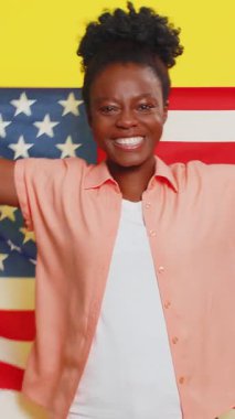 Amerikan bayrağını sallayıp saran mutlu Afrikalı Amerikalı kadın insan haklarını ve özgürlüklerini kutluyor. Bağımsızlık Günü. Başkanlık seçimi. Sarı arka planda izole edilmiş genç siyah kız.