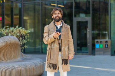 Mutlu Hintli işadamı akıllı telefon yazıcı kullanıyor e-posta mesajlarına cevap veriyor açık havada online mobil uygulamalarla sohbet ediyor. Şehir merkezindeki kameraya bakan Hintli turist. İş adamları