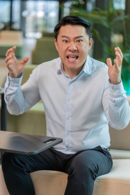 Tişörtlü kızgın yetişkin patron ofisteki modern işyerindeki kameraya bakarak video konuşması yapıyor. Tatminsiz Çinli iş adamı, şirket sorunları hakkında astlarıyla iletişim kuruyor..