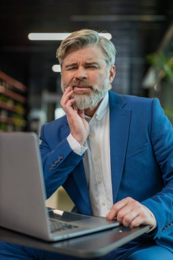 Ofis lobisindeki beyaz iş adamı dizüstü bilgisayarla çalışıyor ve diş ağrısının elinle yanağa değdiğini hissediyor diş hastalığından dolayı acı veren bir ifade. Pulpitis, sakız hastalığı, diş hastalıkları konsepti.