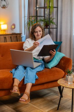 Finansal grafik belgeleriyle çalışan kadın muhasebeci, çizelgeler için vergileri hesaplayan ve kanepenin ev gelirlerinin grafiklerini çizen kadın. Laptop bilgisayarında çalışan genç bir kız, masraflar için bütçe planlıyor. Dikey