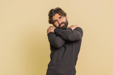 Come to me, I want to embrace you. Indian handsome man spread hands and give hug to you. Pleasant expression, love feelings. Young guy isolated alone on beige studio background. People lifestyles.