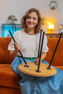 Mutlu beyaz kadın evde mobilya montajını bitiriyor. Başarılı masa tahsilatı, onarım. Yeni daireye taşındıktan sonra genç bir kız. Mobilya mağazasının reklamı. Dikey.