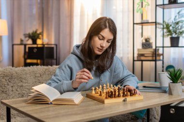 Tek başına satranç oynayan genç bir kadın koltukta oturmuş odaklanmış bakarken taşları düzenliyor. Kız çalışmaları yakınlardaki satranç kitaplarından hareket ediyor. Derin düşüncelere dalmış bir sonraki stratejik adımı planlıyor.