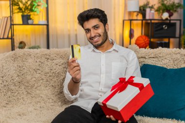 Evde kredi kartı tutan Hintli heyecanlı bir adam, online alışveriş yapıyor, ödeme onayını bekliyor. Kanepedeki Arap genç adam beklenmedik bir hediye teslim aldıktan sonra şaşırdı ve heyecanlandı.