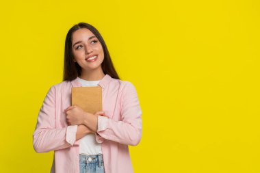 Genç kadın nazikçe gülümsüyor, kitabı kapatıyor okuduktan sonra tatmin edici bir duygusal tepkiyle göğsüne bastırıyor. Sarı arka plandaki kız sıcaklığını ifade eder. Yürekten hikâyeye dokunmanın verdiği neşe.