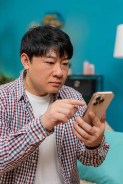 Kanepede oturan Asyalı adam akıllı telefondan internet formunu dolduruyor. Dikkatlice ekrana dokunuyor ve ciddi bakışlar atıyor. Çinli adam dijital uygulama sırasında hataları önlemek için özenli konsantrasyon gösteriyor.