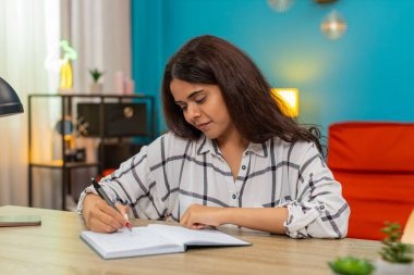 Evde oturan Hintli kadın deftere notlar yazıyor sonra da dikkatle odaklandığını ve öğrendiğini gösteren satırları tekrar okuyor. Masada çalışan Arap bir kız içerik incelemesi yaptı. Ayrıntıları gözden geçirdi. Anlayış ve ustalık sağladı..