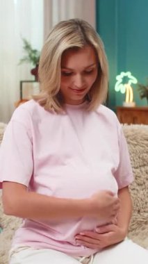 Hamile, orta yaşlı bir kadın karnının üzerinde elleri ile kalp oluşturur. Yavaşça gülümser ve doğum için beklenti hisseder. Kafkasyalı kız kanepeye uzanmış, nazik bir anın tadını çıkarıyor. Yakında bebeğe sessiz bir aşk yolluyor..