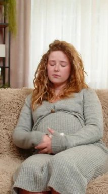 Hamile, üzgün bir kadın, evinde, kanepeye oturup nazikçe karnını tutar, duygusal ifadeyle gözyaşlarını siler, duyarlı ve düşünceli hisseder. Kız anneliğin zorluklarını ve derin duygularını benimsiyor..